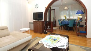 Una sala de estar con sofá, televisión, aparador de madera y comedor con mesa y sillas.