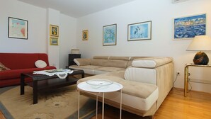 Una sala de estar con un sofá rojo, un sofá color beige, una mesita redonda y una lámpara. Hay cuadros enmarcados en las paredes.