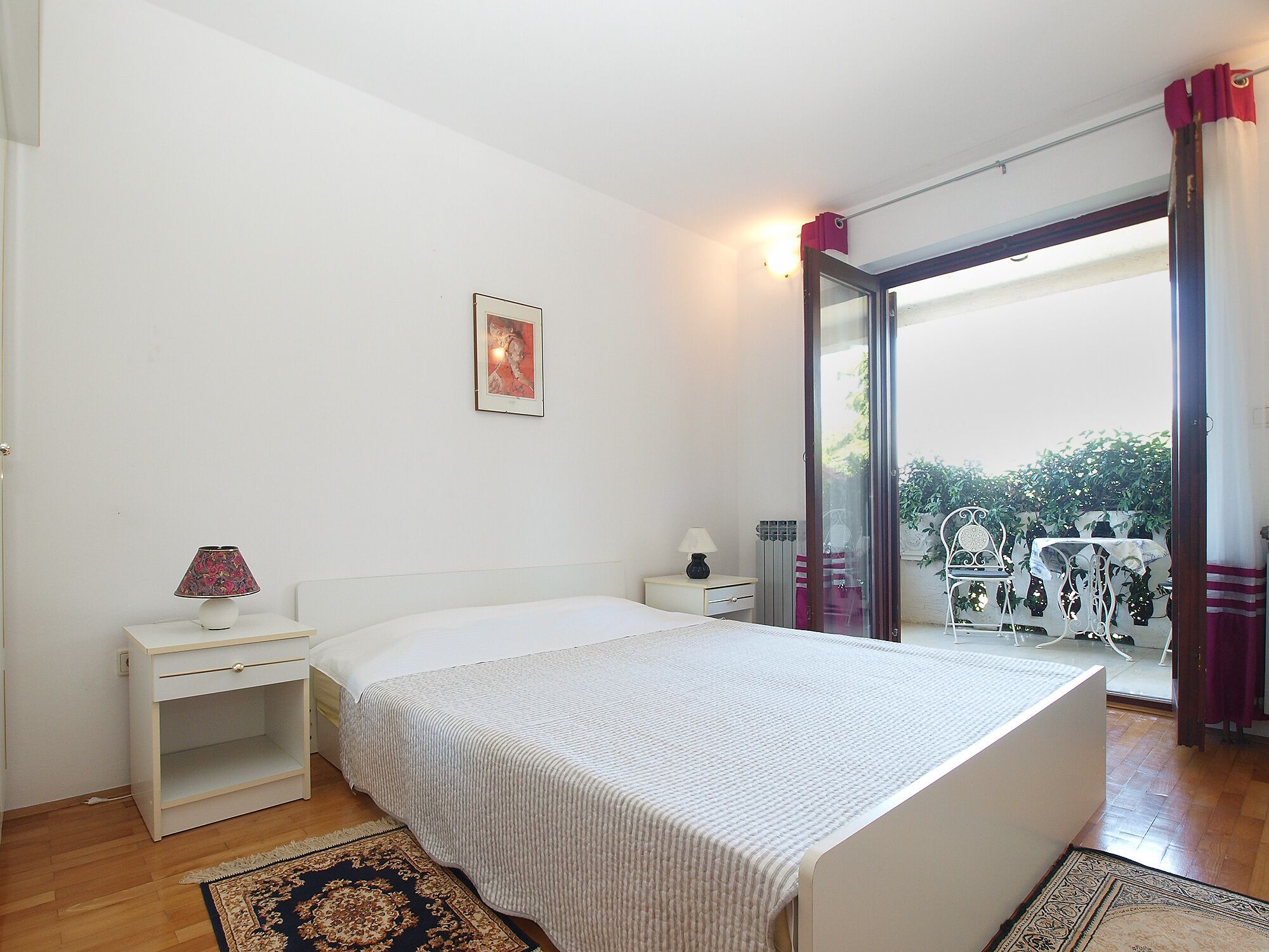A bedroom with a bed, bedside table, lamp, and a view of the outdoors through a glass door.