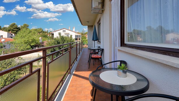 A balcony with a table and chairs, a potted plant, and a view of the surrounding area. - Apartment 1947 (Fazana)