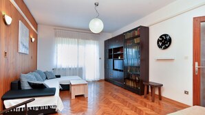 A modern living room with a sofa, a small table, a bookshelf, and a large window with curtains. - Apartment 1947 (Fazana)