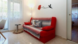 Un salon avec un canapé rouge, une petite table d’appoint et une lampe.