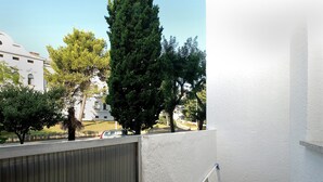 Un balcon doté d’une rambarde en métal, d’un banc en bois et offrant une vue sur une rue animée, avec des voitures et des immeubles.