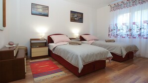 Une chambre avec deux lits, un plancher en bois, un tapis rouge et deux lampes fixées au mur.