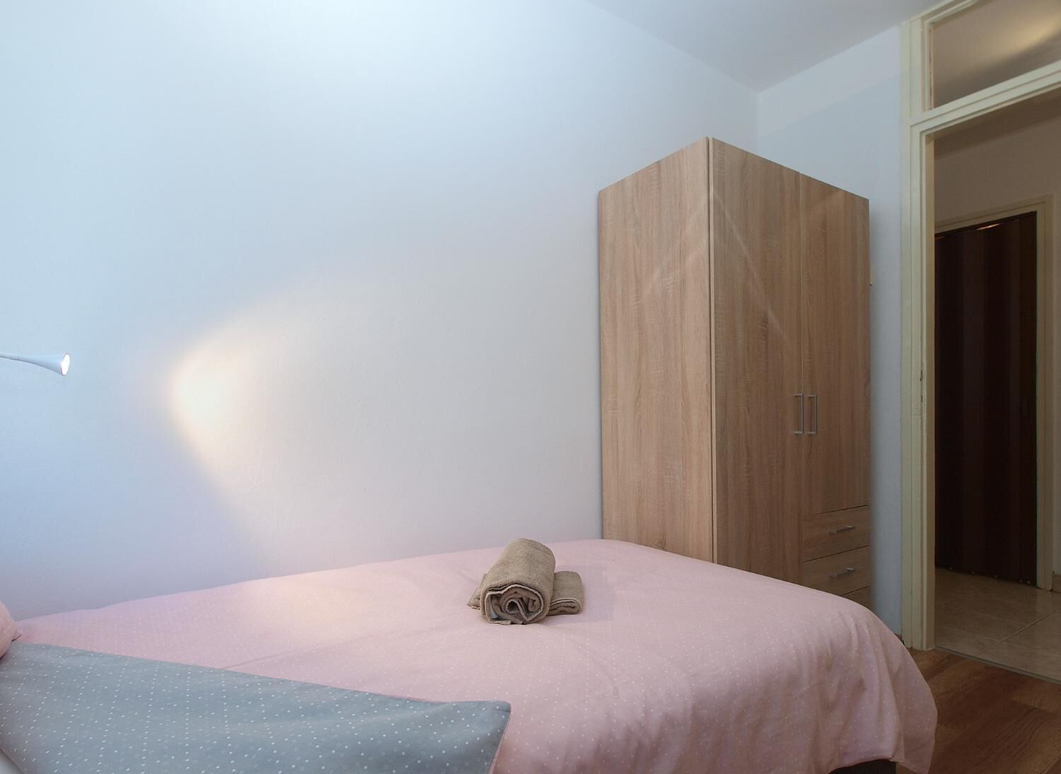 A bedroom with a bed, a wooden wardrobe, and a door leading to another room.