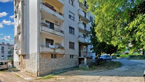 Un immeuble résidentiel à plusieurs étages, doté de balcons, d’une base en pierre et d’une allée pavée.