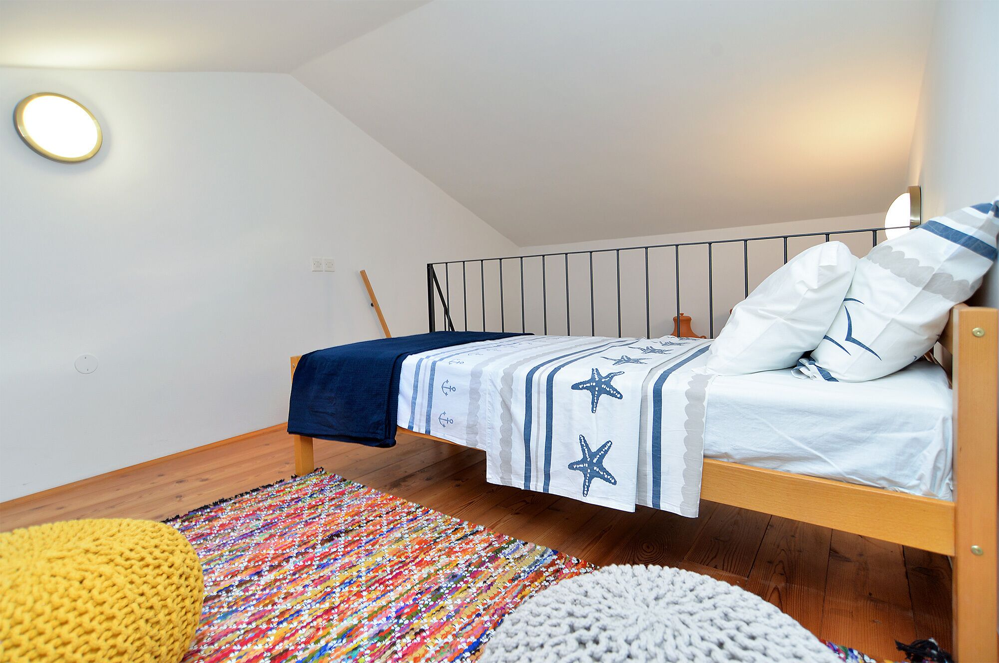 A bedroom with a bunk bed, a colorful rug, and a white wall with a light fixture.