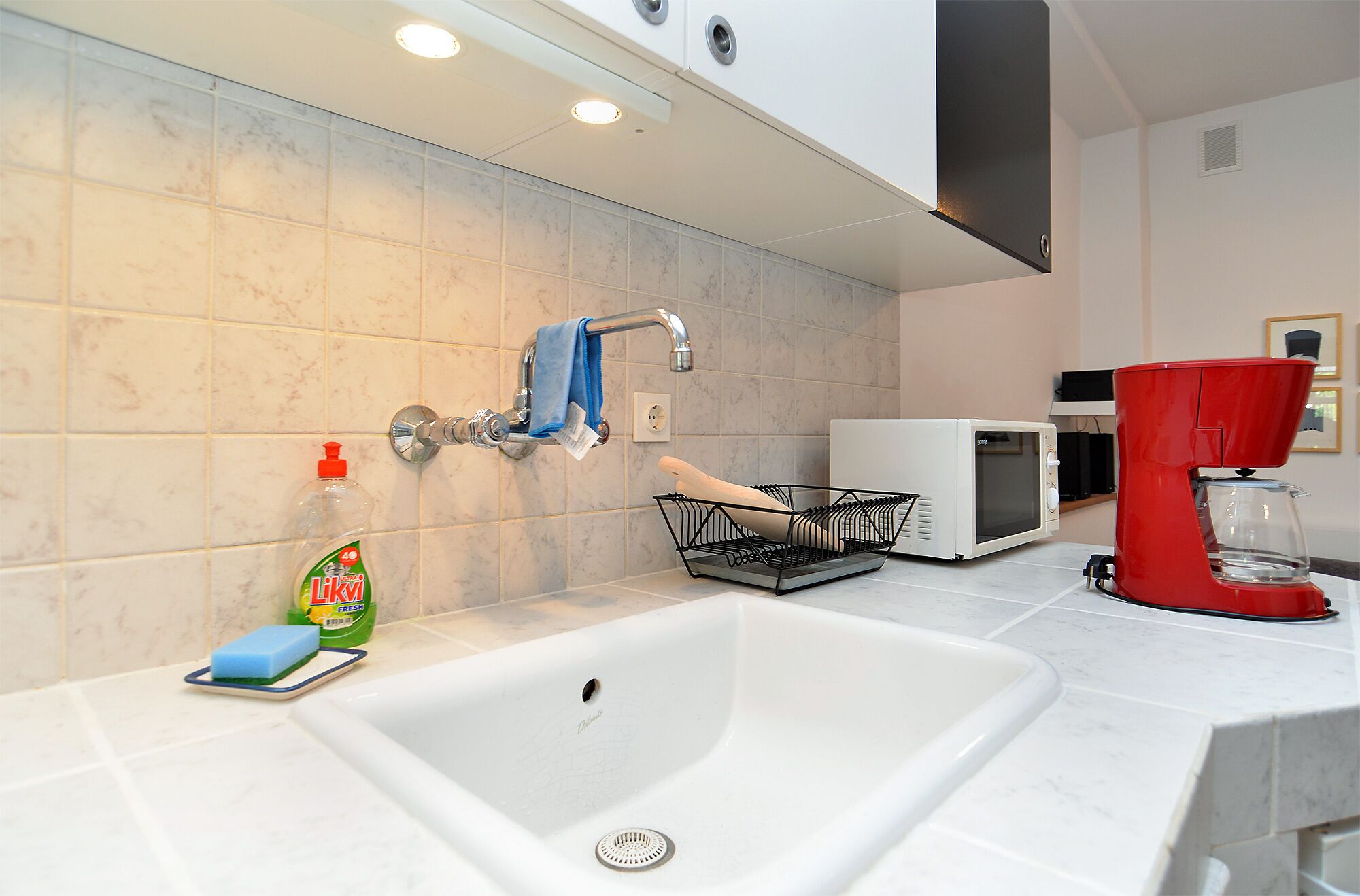 A kitchen with a white sink, a microwave, a red coffee maker, and a dish rack.