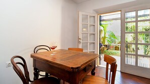 Een eethoek met een houten tafel en stoelen, een wijnglas, en uitzicht door een glazen deur op een tuin.