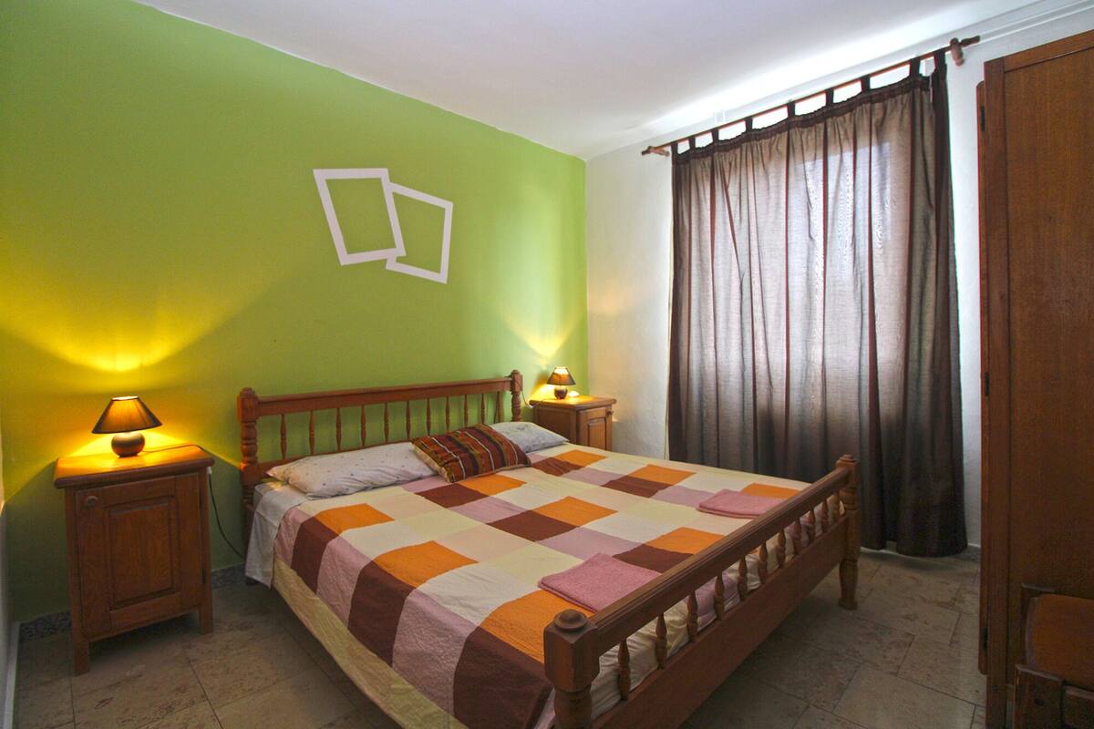 A bedroom with a wooden bed, green walls, two bedside lamps, and a window with curtains.