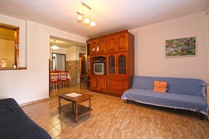 A living room with a blue sofa, a wooden cabinet, a small table, and a television. - Apartment 1954 (Fazana)