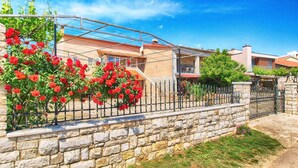 A residential area with stone walls, a metal fence, and red flowering plants. - Apartment 1954 (Fazana)