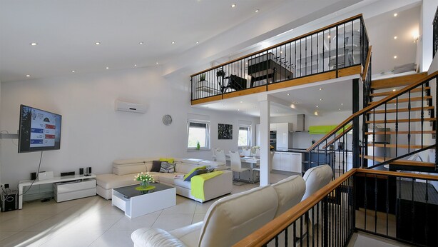 Un vaste espace de vie au design moderne, comprenant un plafond haut, un escalier avec une rampe en bois et une cuisine ouverte sur le reste de la pièce.