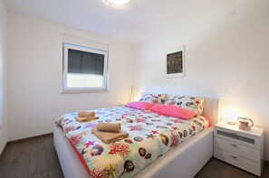 A bedroom with a bed, a nightstand, a window, and a wall-mounted picture.
