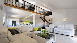 Un vaste espace de vie doté d’un haut plafond, une cuisine à l’arrière-plan et un escalier menant à un niveau supérieur.