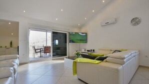 Un salon moderne avec un canapé blanc, un téléviseur fixé au mur et une porte-fenêtre coulissante donnant sur un balcon.