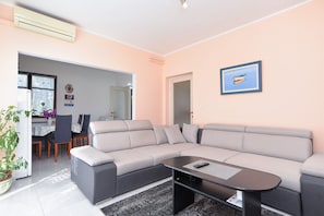 Ein modernes Wohnzimmer mit einem grauen Ecksofa, einem schwarzen Couchtisch und einem Essbereich im Hintergrund.