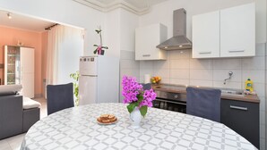 Una cocina moderna con armarios blancos, una campana extractora de acero inoxidable y una mesa redonda con mantel estampado.