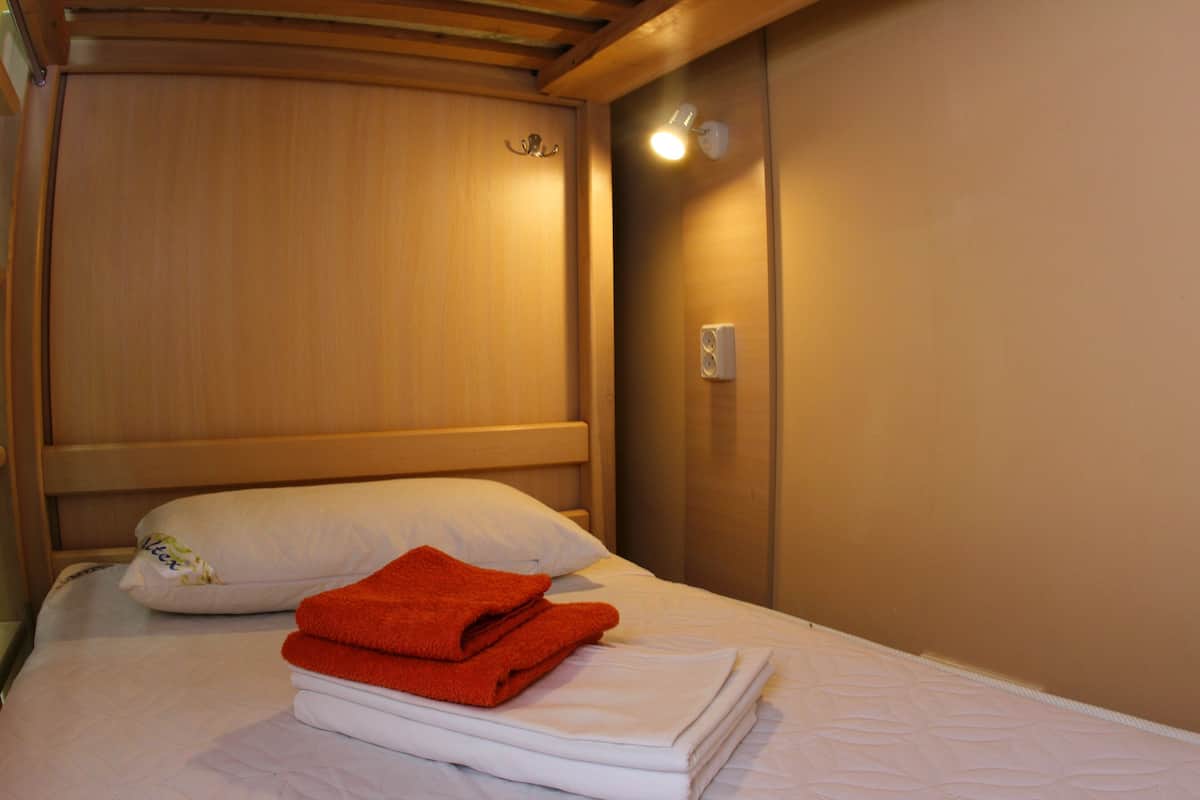 Un letto rifatto con asciugamani bianchi e arancioni, una testiera in legno e un faretto a parete.