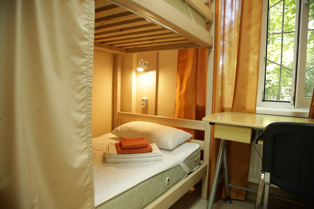Un letto a castello con scrivania e sedia, una finestra con tende e una lampada da comodino.