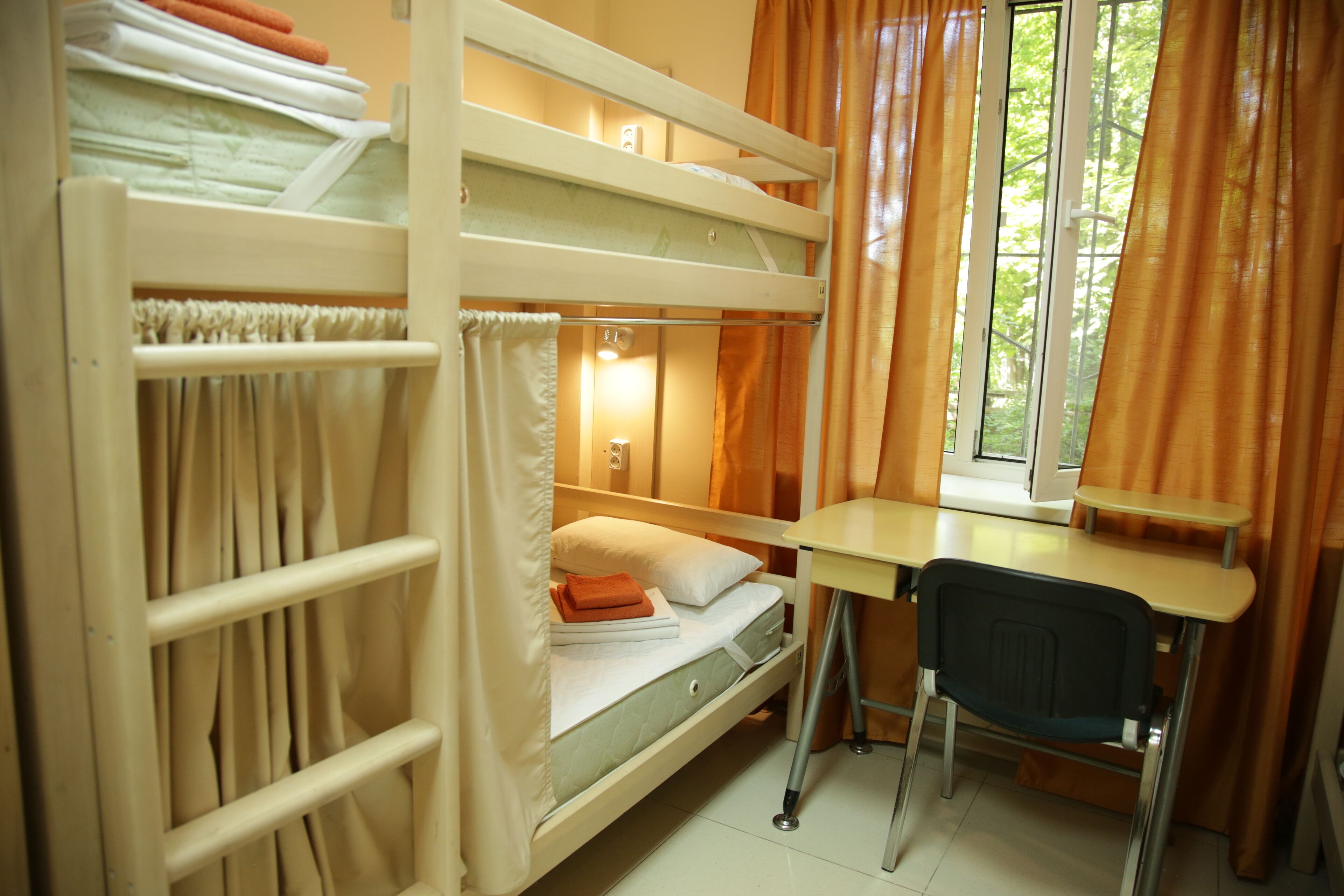 A bunk bed room with a desk and chair, curtains, and a window with a view.