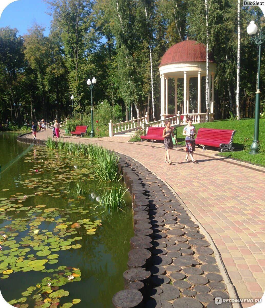 A gazebo with a red roof and white columns, surrounded by a brick pathway and benches.