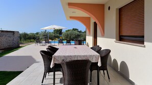 Une terrasse extérieure avec une table et des chaises, une piscine en arrière-plan et un mur en pierre.