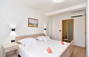 Ein Hotelzimmer mit Bett, Nachttischen, einem Gemälde, einem Spiegel und einer Klimaanlage.