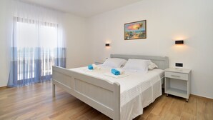 Une chambre à coucher avec un lit, des tables de chevet, un tableau et une fenêtre ornée de rideaux légers.