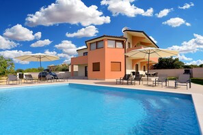 Ein modernes, zweistöckiges Haus mit Swimmingpool, Sitzgelegenheiten im Freien und blauem Himmel.