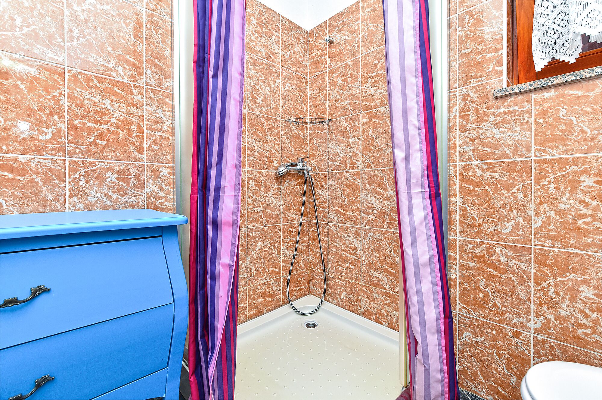 A bathroom with a shower, tiled walls, and a blue cabinet.