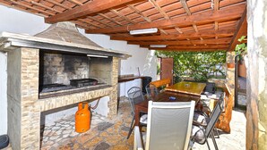 An outdoor patio with a stone fireplace, a wooden table, and metal chairs. - House 1962 (Vodnjan)