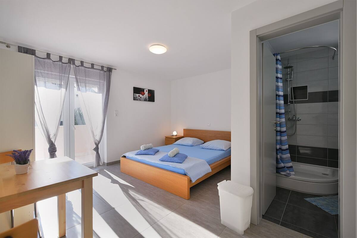 A bedroom with a bed, bedside table, and a shower area.