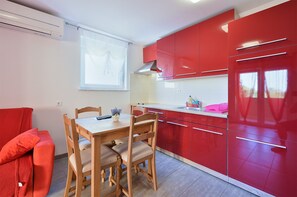A compact kitchen with red cabinets, a wooden dining table, and a window providing natural light.