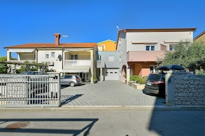 A residential street with houses, a gated driveway, and parked cars.