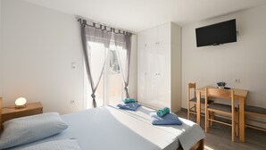 A bedroom with a bed, a desk, a chair, a TV, and a window with curtains. - Apartment 1964 (Medulin)