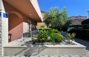 A building with a pink facade, a gated entrance, and a landscaped garden area with various plants and a small water feature.