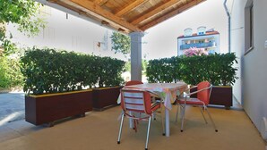 Une terrasse extérieure dotée d’un plafond en bois, d’une table avec des chaises et de plantes en pot.