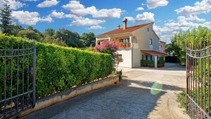 Une maison avec un toit recouvert de tuiles rouges, un jardin bordé d’une haie et un portail.