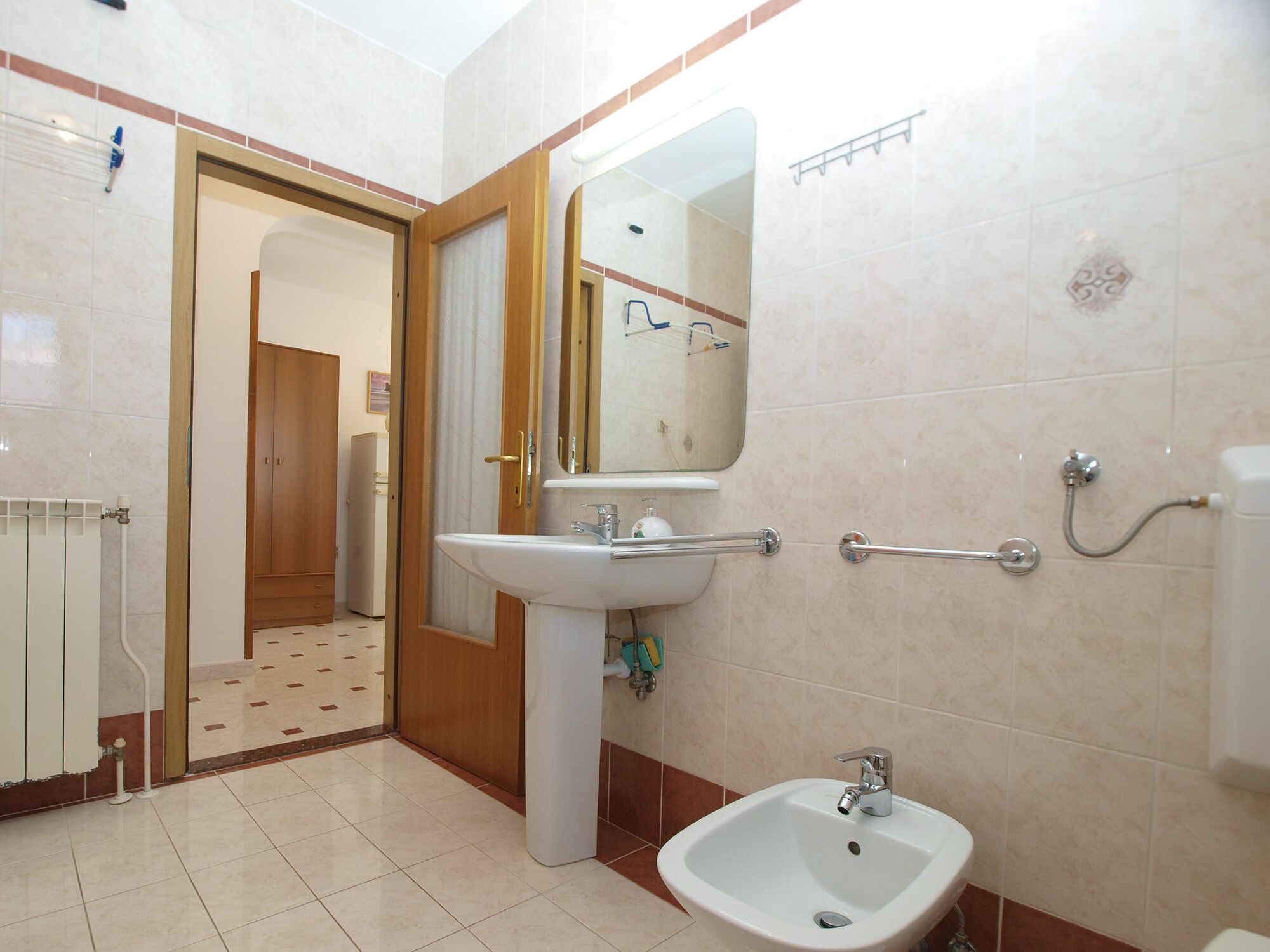 Une salle de bain avec un lavabo, un bidet et un miroir. Une porte donne accès à une autre pièce.