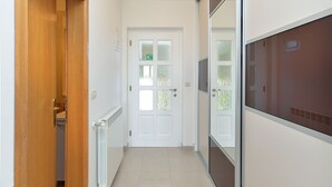 A narrow hallway with a wooden door on the left, a white door with frosted glass panels in the center, and a large window on the right. - Apartment 1966 (Umag)