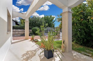 A covered outdoor area with a tiled floor, potted plants, and a metal gate. - Apartment 1966 (Umag)