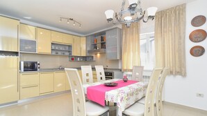 A modern kitchen with yellow cabinets, a microwave, and a dining area with a pink tablecloth. - Apartment 1966 (Umag)
