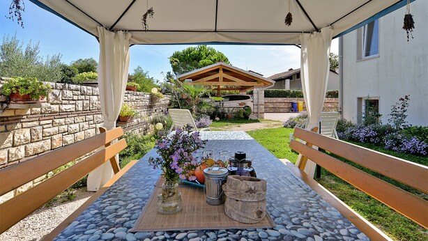 An outdoor patio with a table set for dining, surrounded by stone walls and potted plants. - Apartment 1966 (Umag)