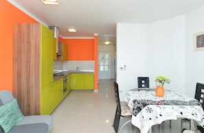 Una cucina moderna con pareti color arancione acceso, una zona pranzo con tavolo e sedie, e una porta che dà su un'altra stanza.