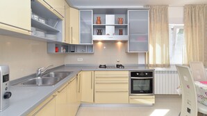 A compact kitchen with a gas stove, oven, and a built-in dishwasher. It features light-colored cabinets and a window with curtains. - Apartment 1966 (Umag)