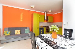 A compact living space with a grey sofa, a dining table with a black and white floral tablecloth, and a vase with a plant. - Apartment 1966 (Umag)