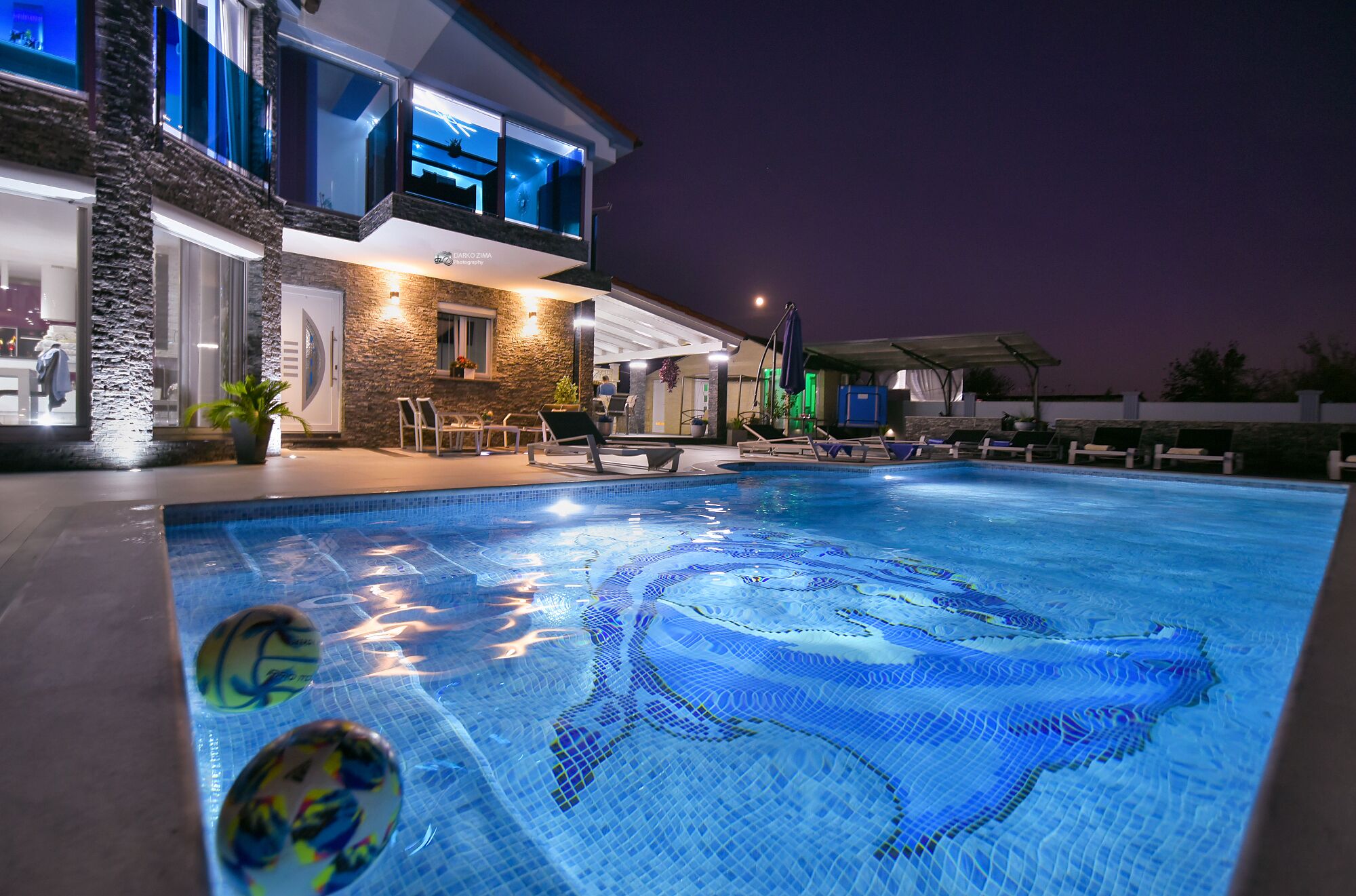A swimming pool with a dolphin design, lounge chairs, and a building with stone facade and large windows.