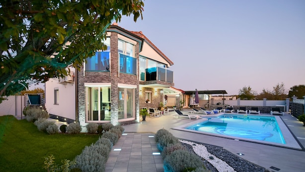 A modern two-story house with a swimming pool, outdoor seating, and a well-maintained garden.