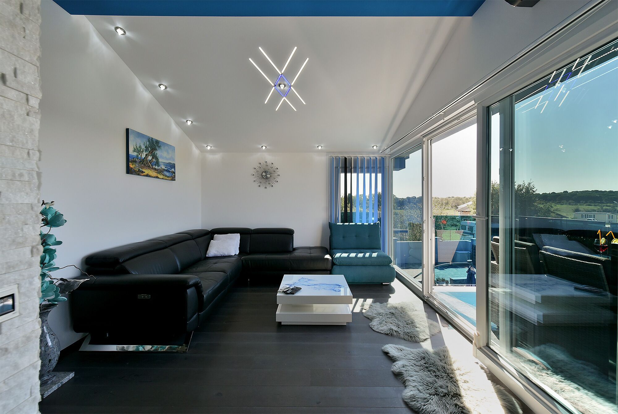Una sala de estar moderna con un sofá de cuero negro, una mesa de centro blanca y un amplio ventanal con vistas a una piscina y un paisaje.